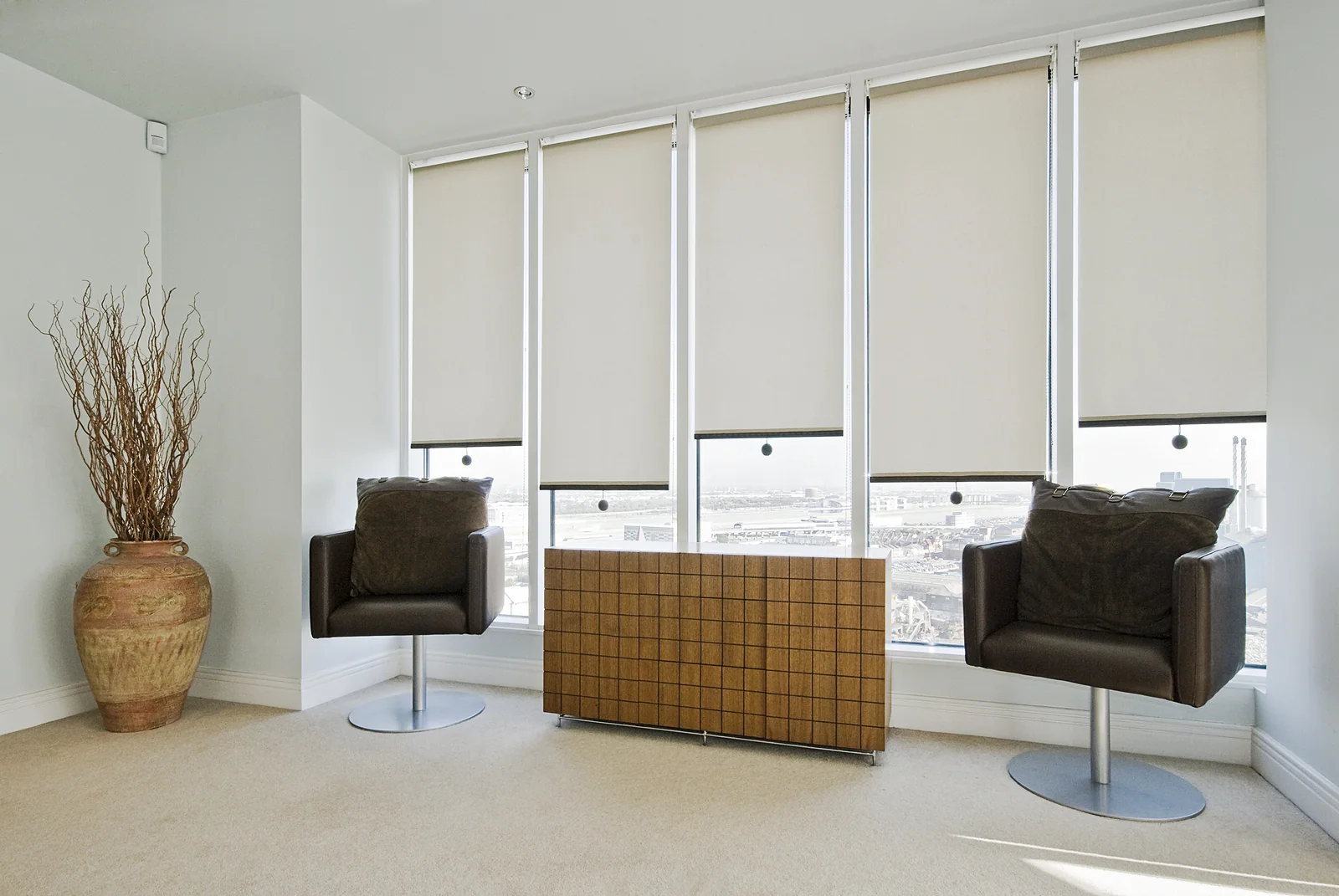 Neutral roller blinds across the windows of a minimal living room